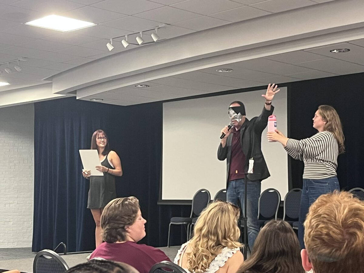 Two students stand onstage next to a blindfolded mentalist performer